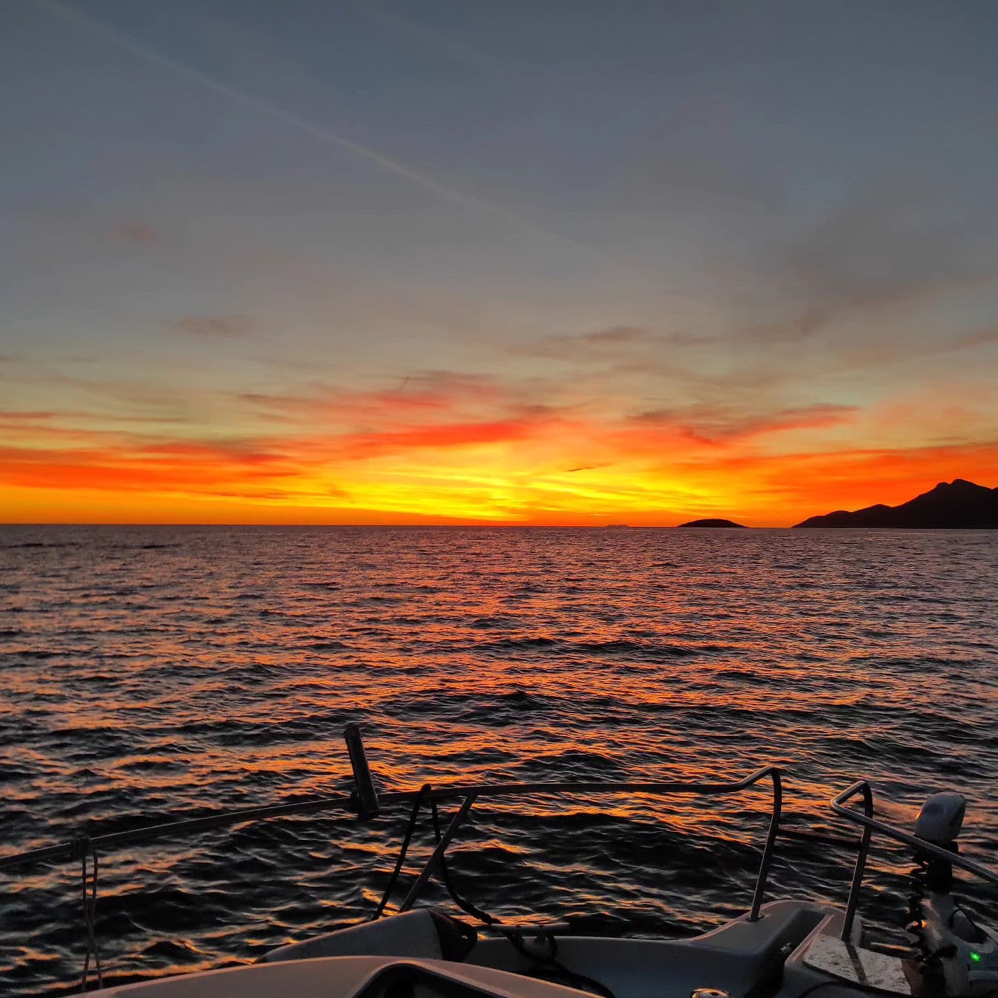 The sun setting over the open sea, seen from the bow of the boat