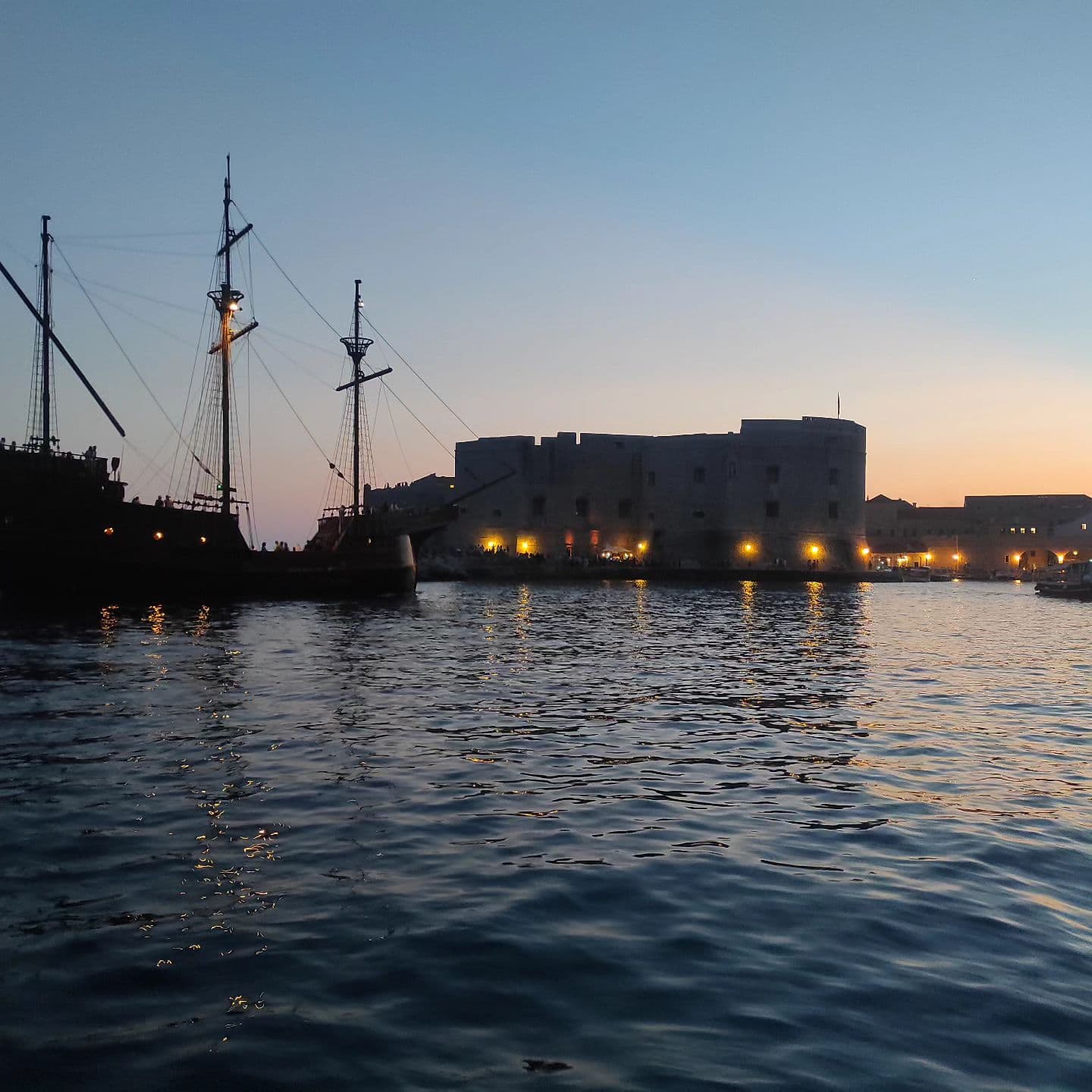 Stara luka Dubrovnika u sumrak s jedrenjakom i osvijetljenim zidinama